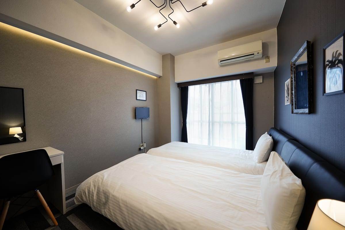 A hotel room with a bed, desk, chair, and a window with curtains.