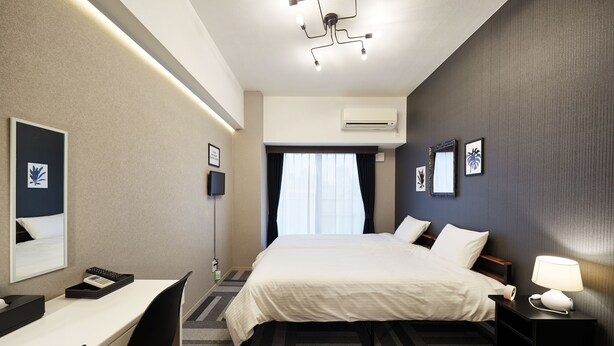 Una habitación de hotel con cama, mesita de noche, escritorio, silla e iluminación en el techo.