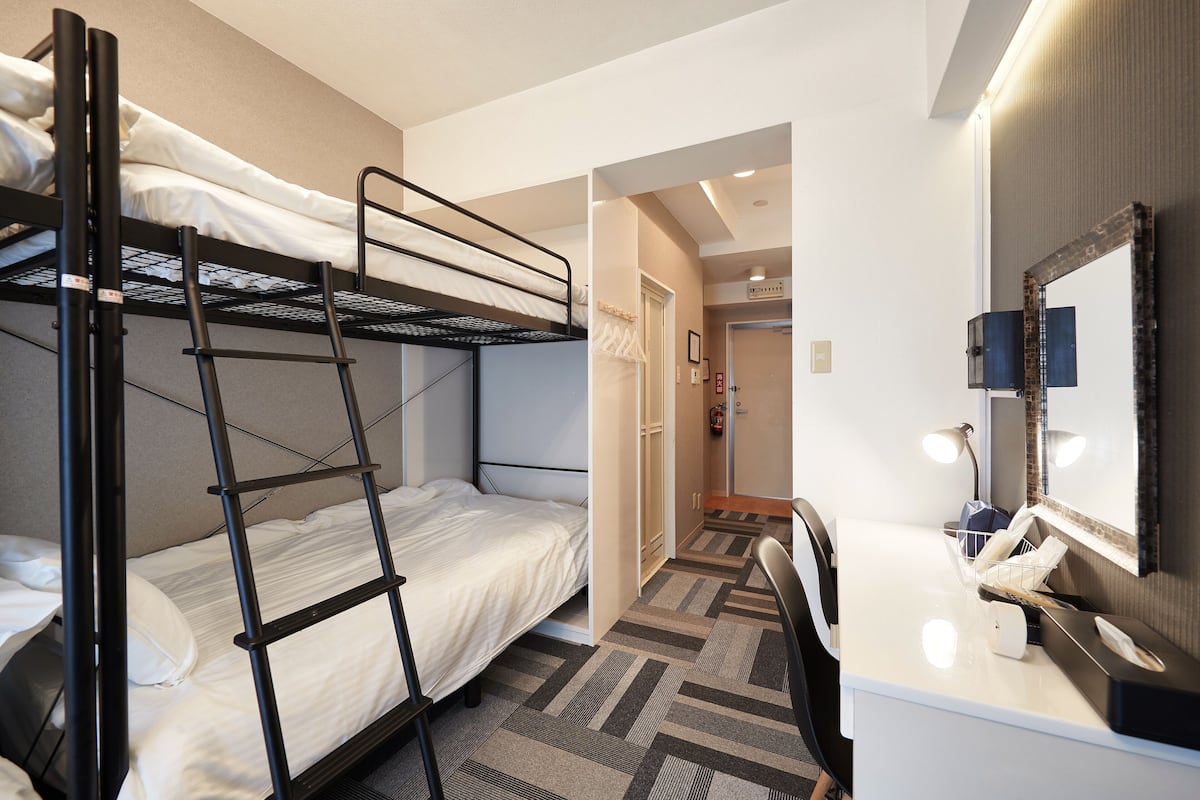 A hotel room with bunk beds, a desk with a mirror, and a small bathroom.