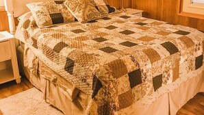 Un lit avec une couette, une table de chevet, une lampe, un tableau encadré au mur et une fenêtre avec des stores.
