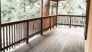 Une terrasse en bois couverte, dotée d’une rambarde et entourée d’arbres.
