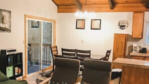 Un salon chaleureux avec des poutres en bois, un coin repas avec une table et des chaises, et une cuisine avec un plan de travail et des placards.