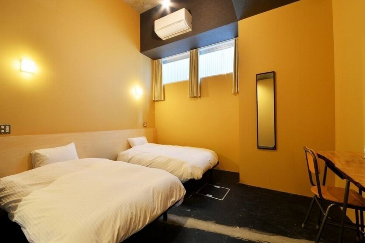 A hotel room with two beds, a desk, a chair, a mirror, and a window with curtains.