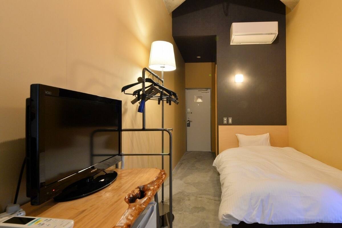 A hotel room with a bed, a TV, a desk with a lamp, and an air conditioner.