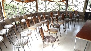 Un espace repas avec des chaises et des tables en métal, de grandes fenêtres à carreaux et un sol carrelé.