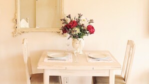 Una mesa de comedor con dos sillas, un jarrón con flores, un espejo y un aplique de pared.