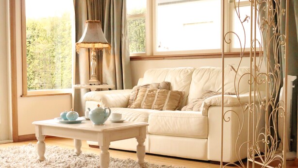 Una sala de estar acogedora con un sofá blanco, una mesita con tetera y tazas, y un atril decorativo de metal.