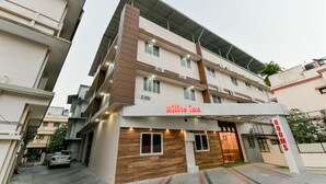 A hotel named 'White Inn' with a modern design, featuring a prominent 'ROOMS' sign, a covered entrance, and a car parked in front. - Hilite Inn (Kanayannur)
