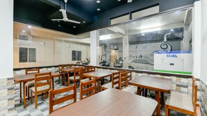 A restaurant with wooden tables and chairs, a ceiling fan, and a view of the street through a glass wall. - Hilite Inn (Kanayannur)
