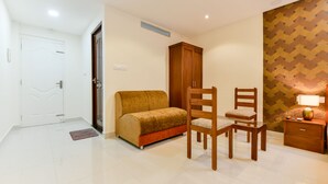 A room with a sofa, two wooden chairs, a small table, a nightstand, and a wardrobe. - Hilite Inn (Kanayannur)