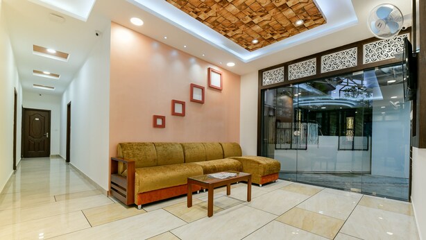 A modern lobby with a beige tiled floor, a brown sofa, and a wooden coffee table. - Hilite Inn (Kanayannur)