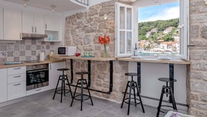 A kitchen with white cabinets, a stone wall, a window with a view of a hillside, and three bar stools.