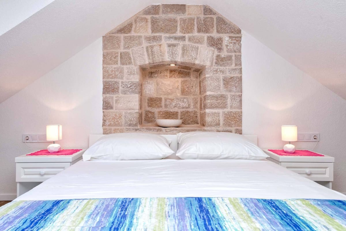 A bedroom with a stone fireplace, white bedding, and bedside lamps.