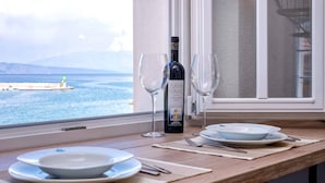A table set with plates, cutlery, and a bottle of Zlatan FavaƧ wine, with a view of the sea and a lighthouse.