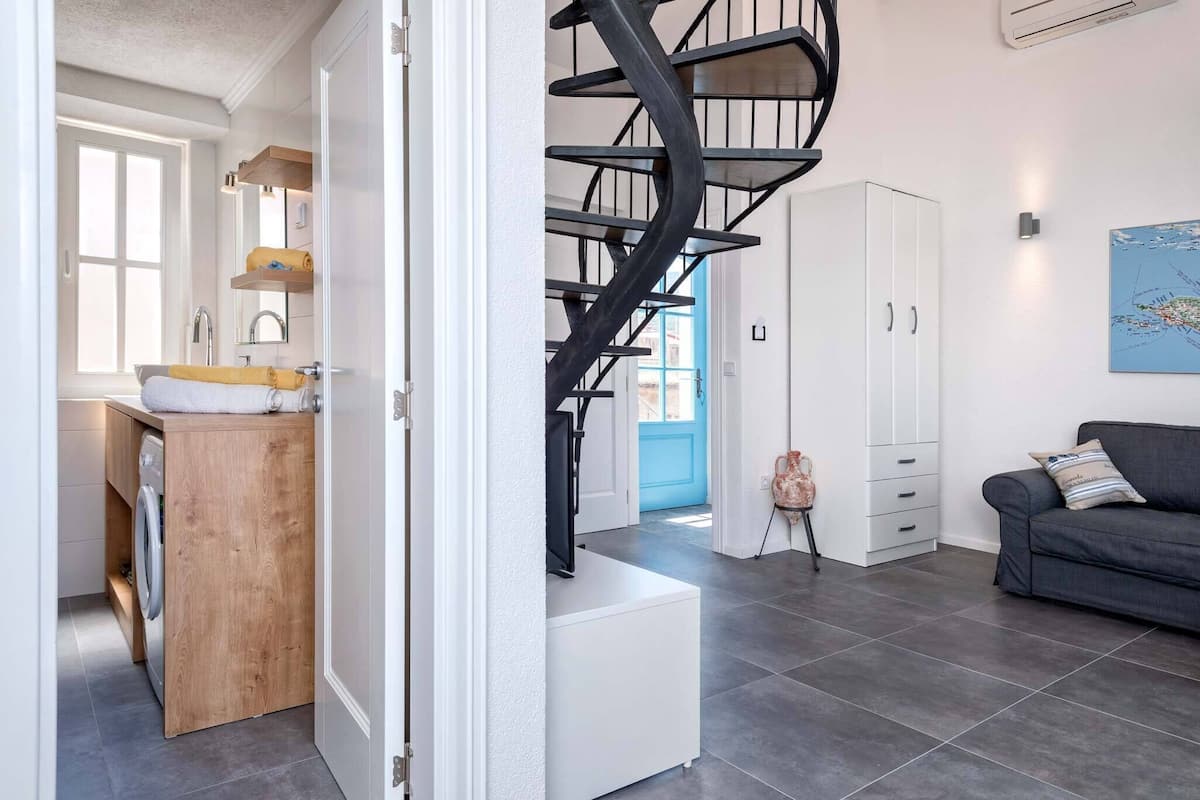 A modern interior with a spiral staircase, a laundry area, and a living room with a sofa and a map on the wall.