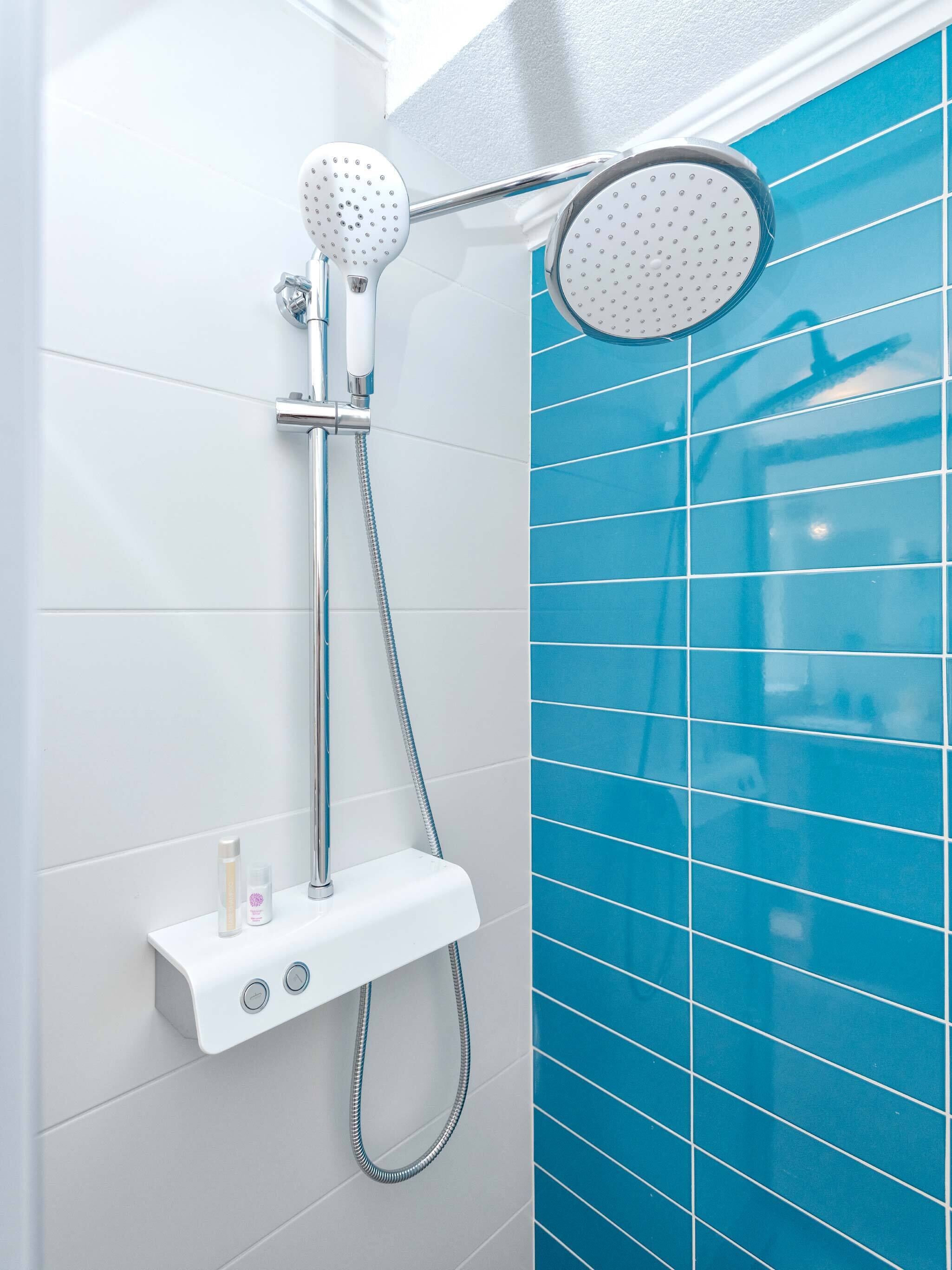 A shower with a handheld showerhead and a wall-mounted rain showerhead, a control panel with two buttons, and a small shelf with toiletries.