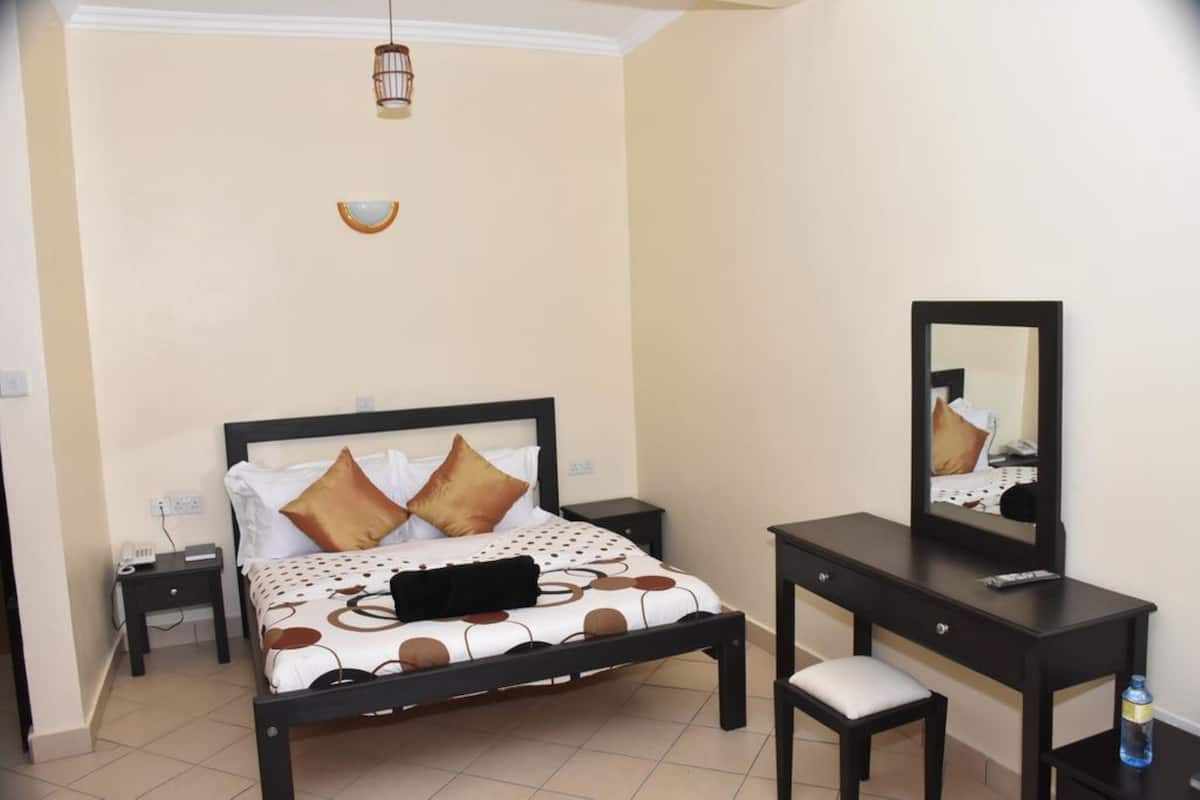 A bedroom with a bed, bedside tables, a desk, and a mirror.