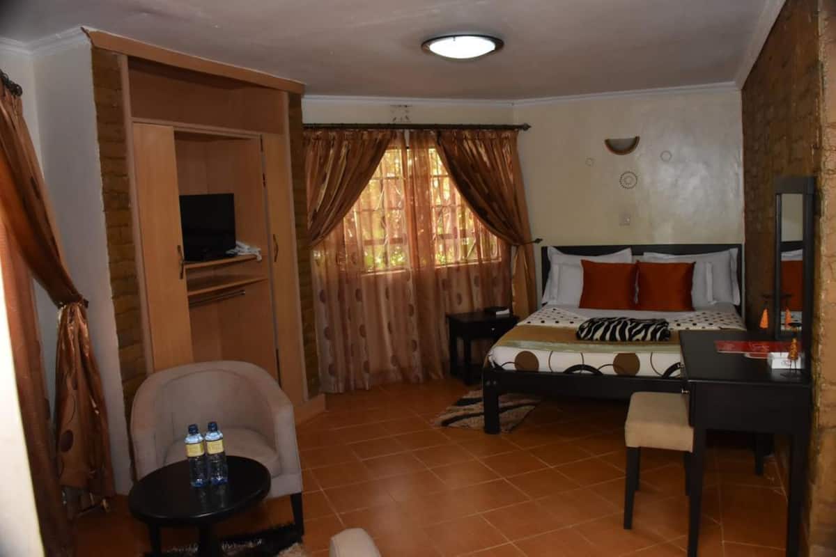 A bedroom with a bed, a desk, a chair, a television, and a window with curtains.