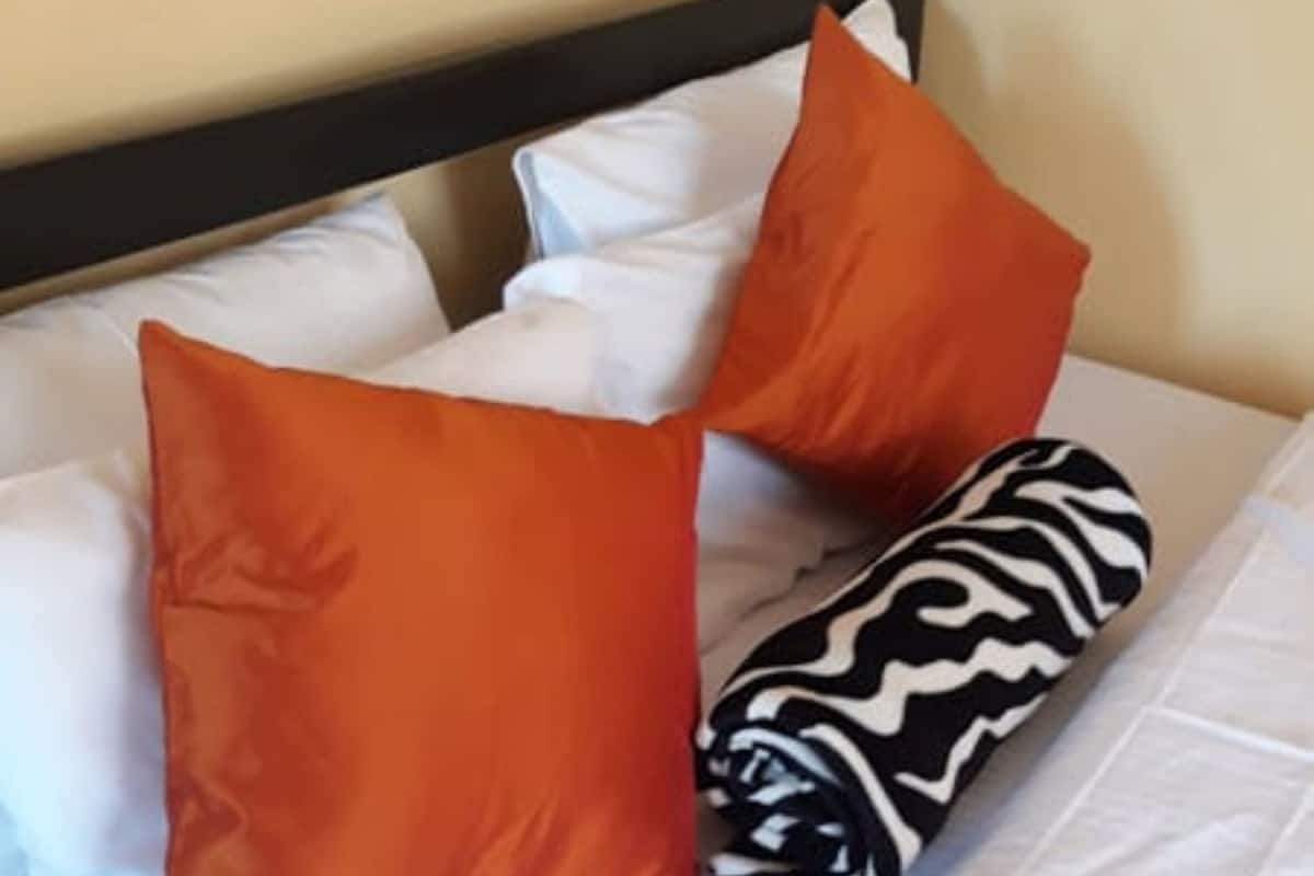 A bed with white bedding, two orange pillows, and a zebra-patterned pillow.