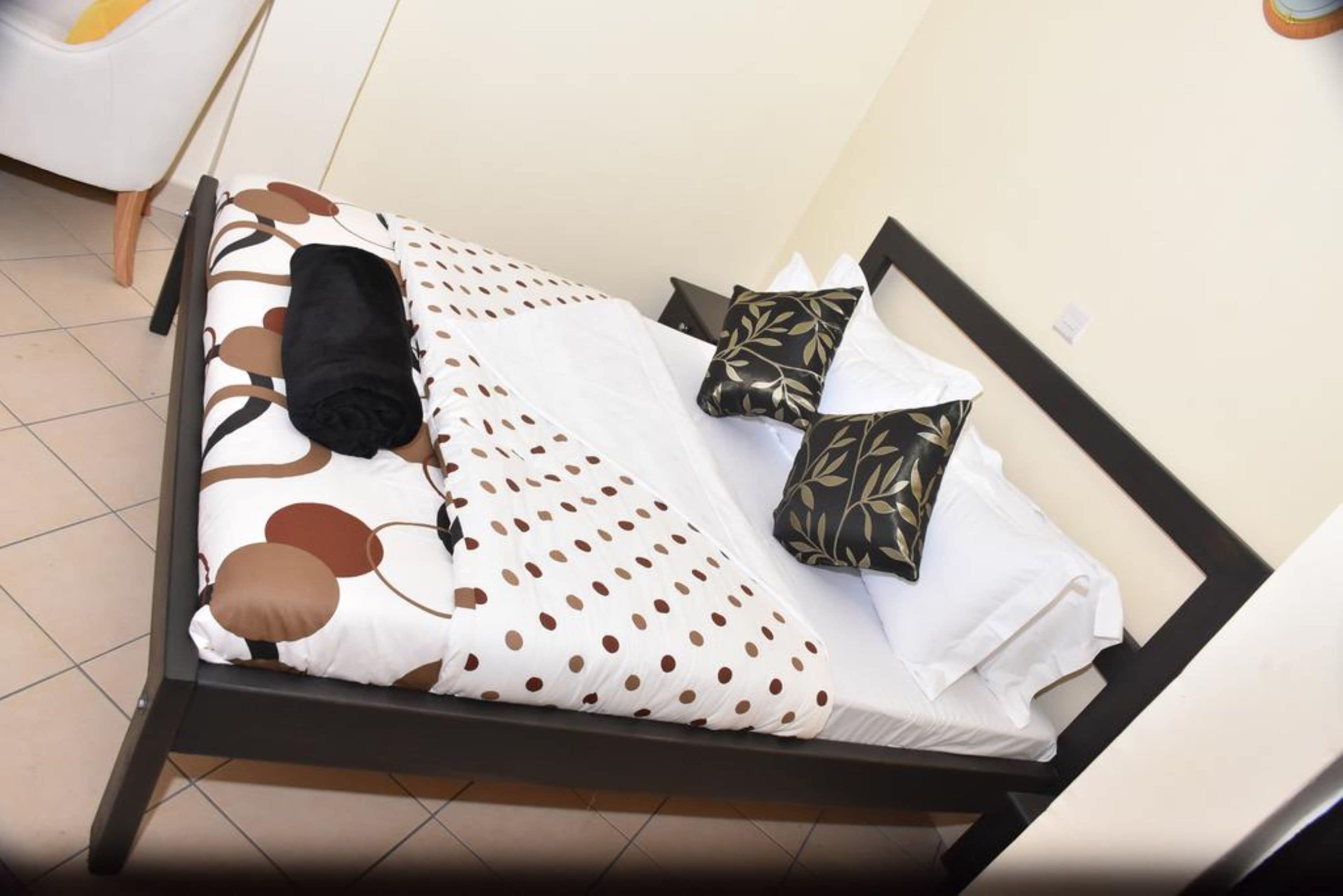 A bed with a white and brown polka dot bedspread, black and gold patterned pillows, and a black blanket.