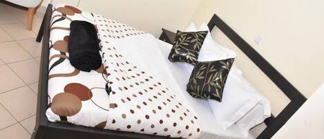 A bed with a white and brown polka dot bedspread, black and gold patterned pillows, and a black blanket.