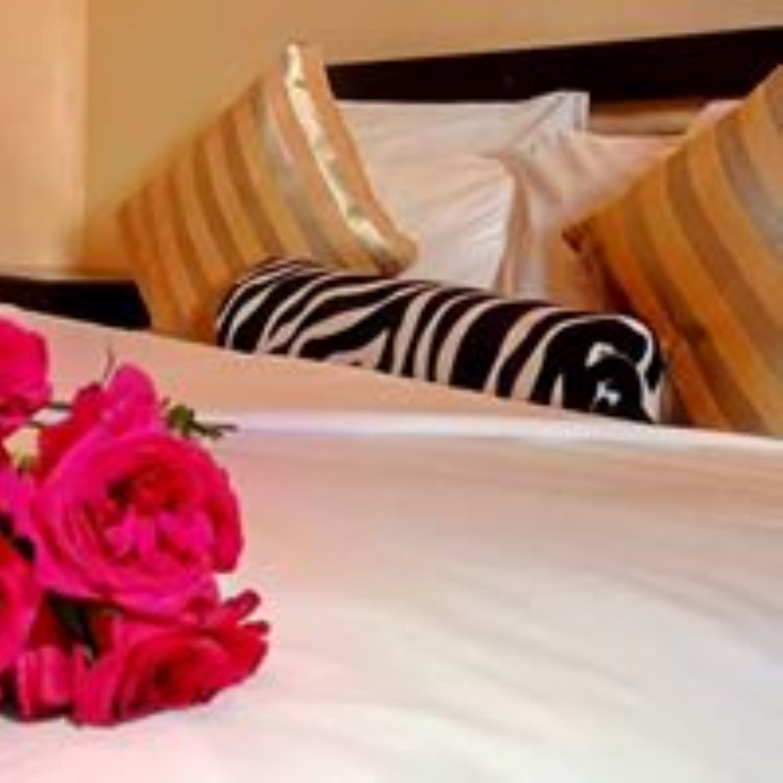 A hotel room with a neatly made bed, striped pillows, and a bouquet of red flowers.
