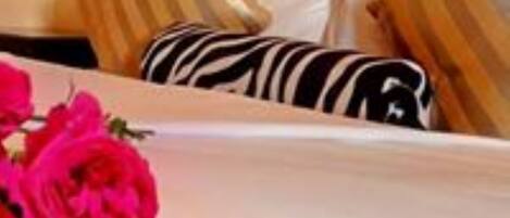 A hotel room with a neatly made bed, striped pillows, and a bouquet of red flowers.
