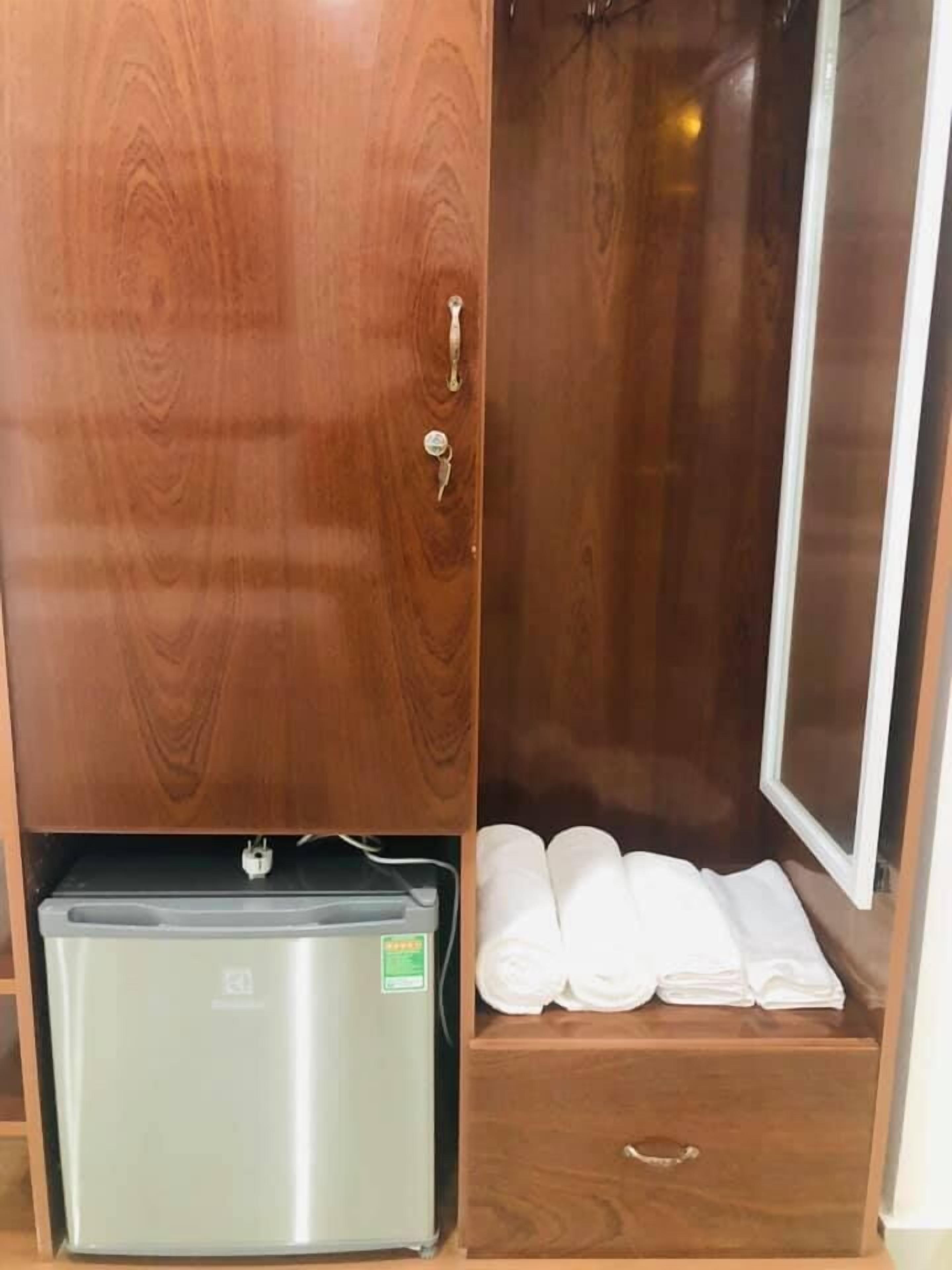 A wooden wardrobe with a small refrigerator and a drawer containing folded towels.