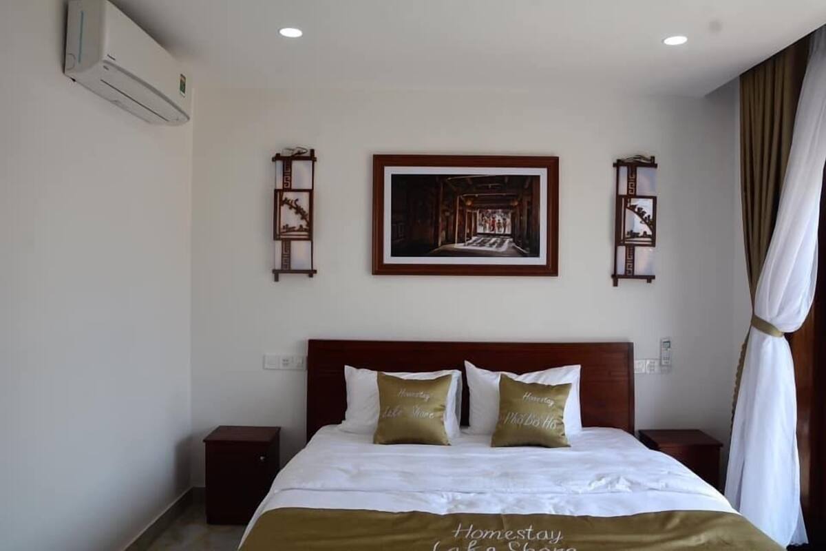 A hotel room with a bed, a nightstand, a framed picture on the wall, and a curtain.