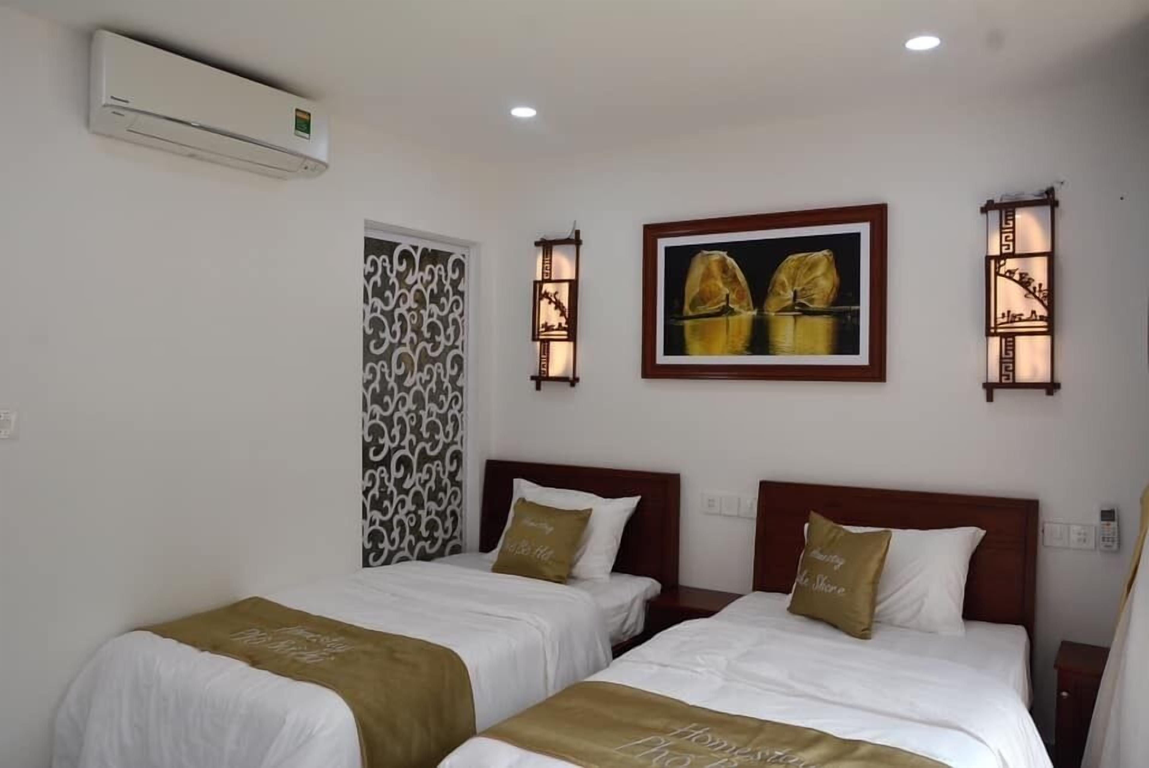 A hotel room with two beds, a wall-mounted air conditioner, decorative wall sconces, and a framed picture.