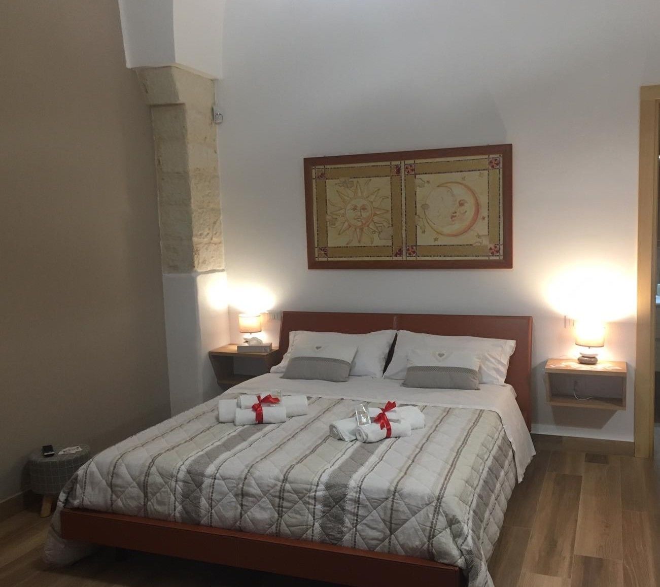 A neatly made bed with a quilted bedspread, two bedside lamps, and a framed artwork above the bed.