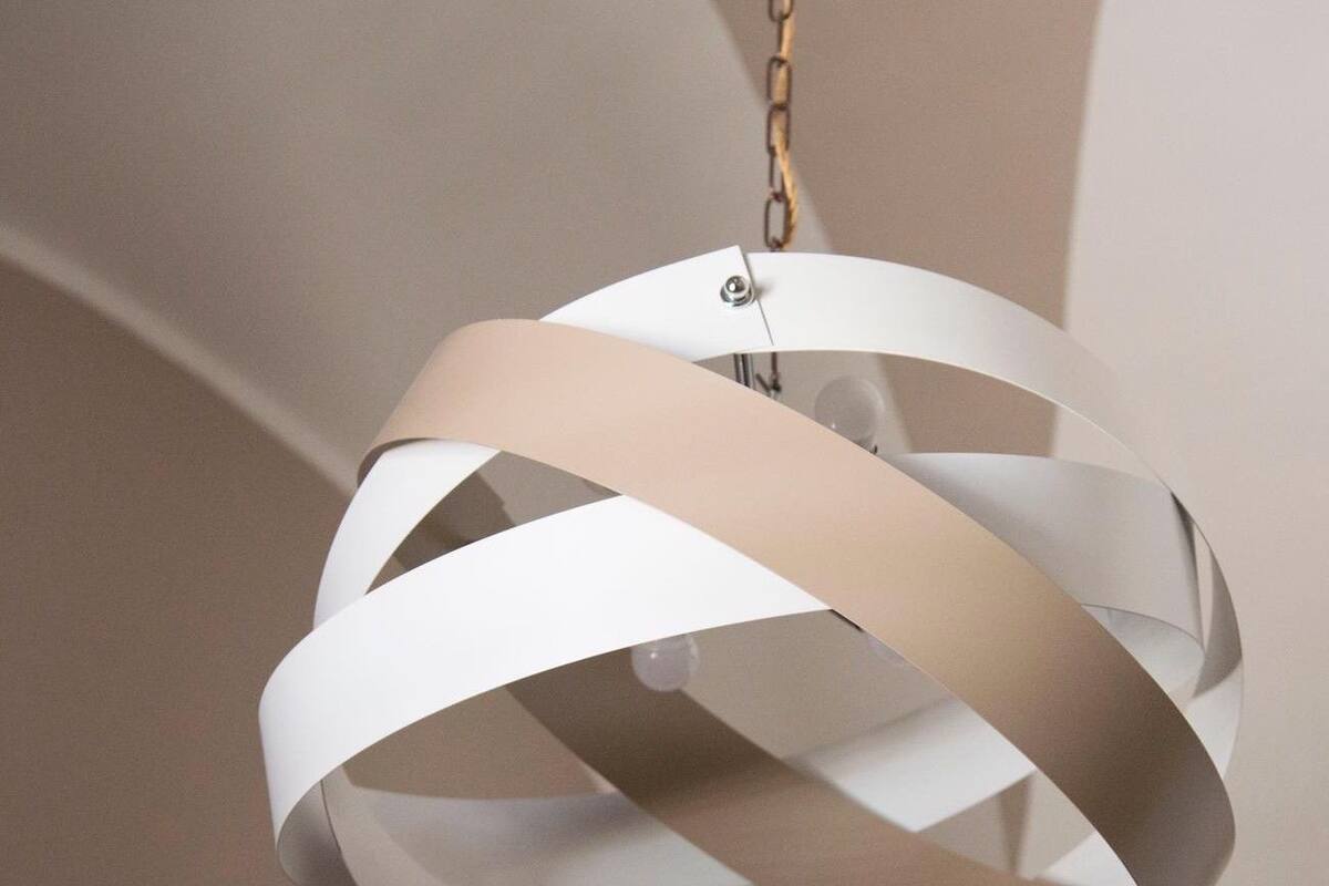 Un luminaire suspendu de forme sphérique et de couleur blanche, doté d’un design minimaliste, et fixé à une chaîne.