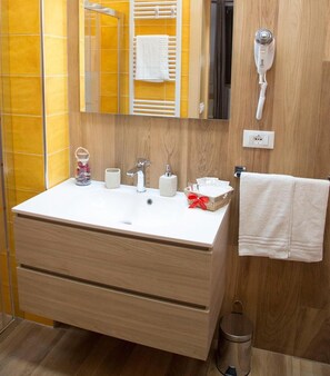 A bathroom with a wooden vanity, a mirror, a hairdryer, and a trash can. - La Dimora di Marco (Melendugno)
