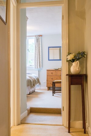 A hallway leading to a bedroom with a window, a dresser, and a vase on a side table. - Wisteria Cottage, Topsham (Topsham)