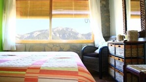 Ein Zimmer mit einem Bett, einem Sessel und einem Fenster mit Blick auf die Berge.
