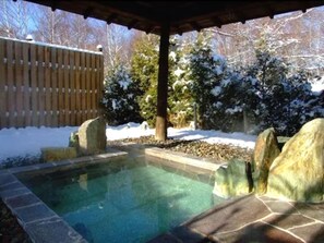 A hot tub area with stone steps leading into the water, surrounded by snow-covered trees and a wooden fence. - Yunokaku Ikedaya (Teshikaga)
