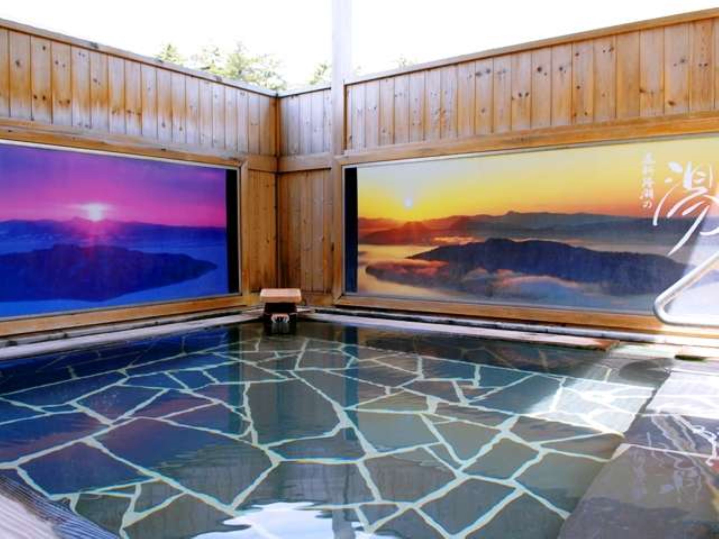 A hot tub with wooden walls and a view of a sunset over mountains.