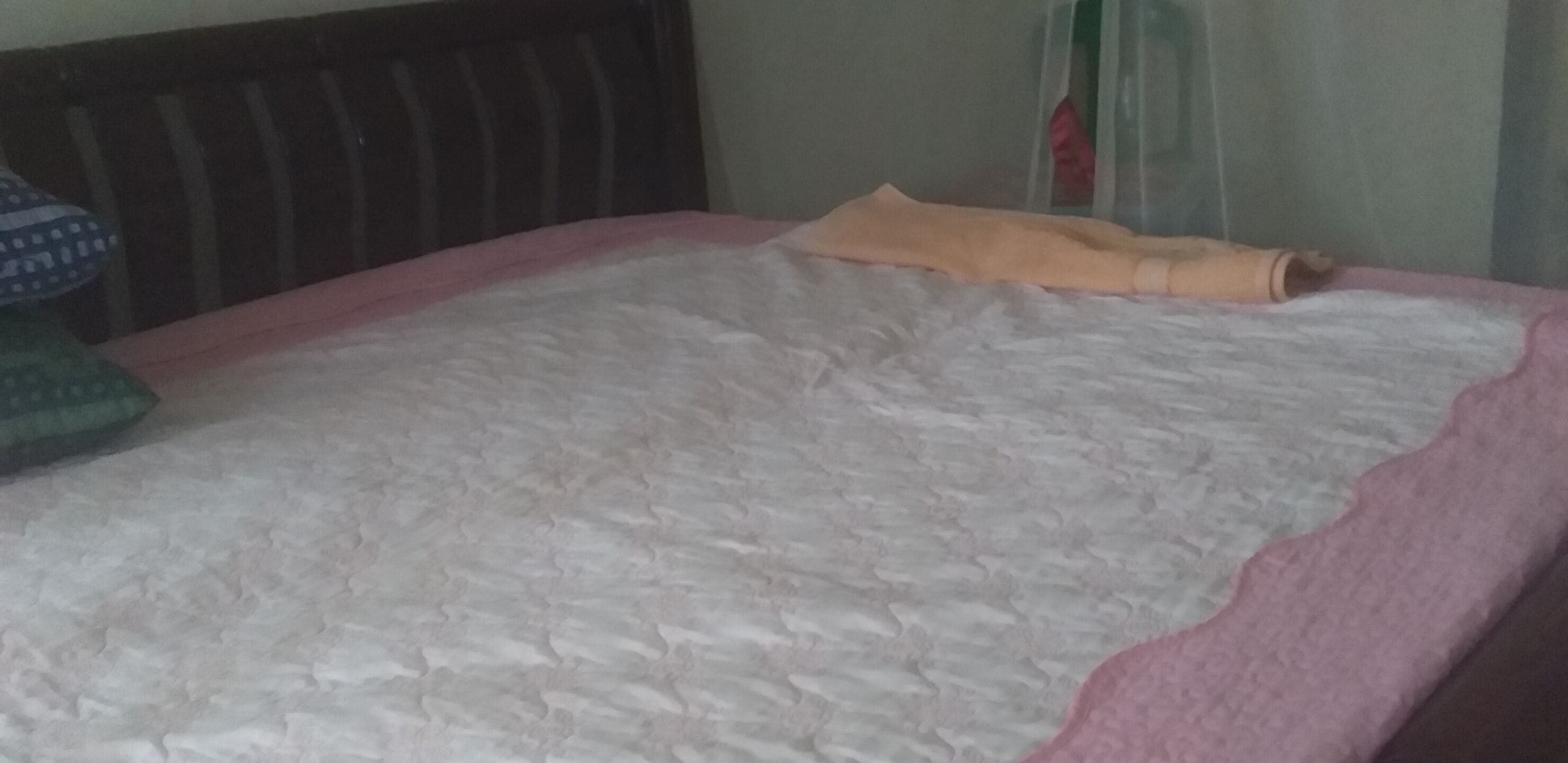A bed with a pink and white quilt, a wooden headboard, and a green pillow.