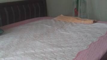 A bed with a pink and white quilt, a wooden headboard, and a green pillow.