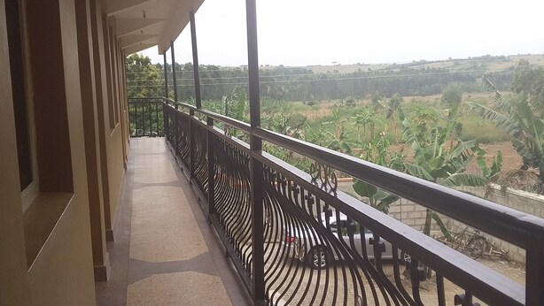 A balcony with a view of a rural landscape, including banana plants and fields. - Elite Lodge (Ntungamo)