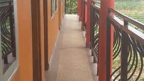 A corridor with red pillars and black railings, leading to a balcony with a view of greenery. - Elite Lodge (Ntungamo)