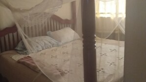 A bed with a canopy, a pillow, and a floral-patterned bedspread. - Elite Lodge (Ntungamo)