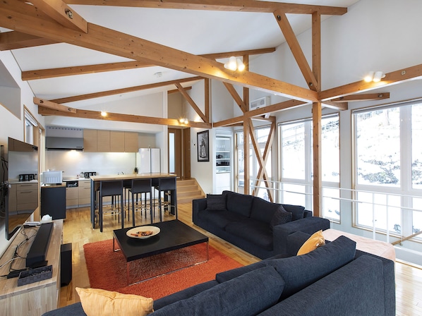 A spacious living area with a dark blue sofa, a wooden ceiling, and large windows. - Casi 67 Chalet (Kutchan)