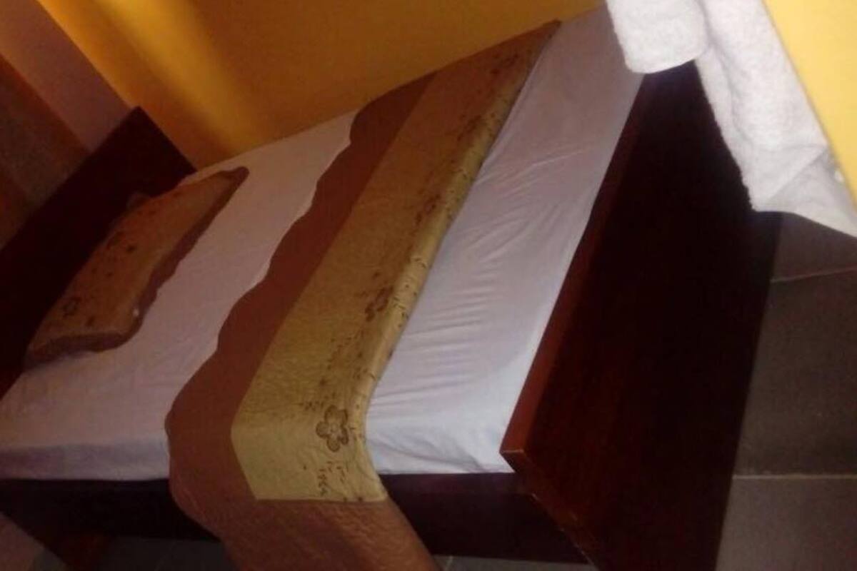 Una cama de madera con un colchón blanco y una manta color beige.