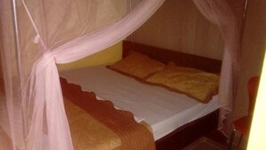 Un lit simple avec un drap blanc et deux oreillers, une tête de lit en bois et une moustiquaire.