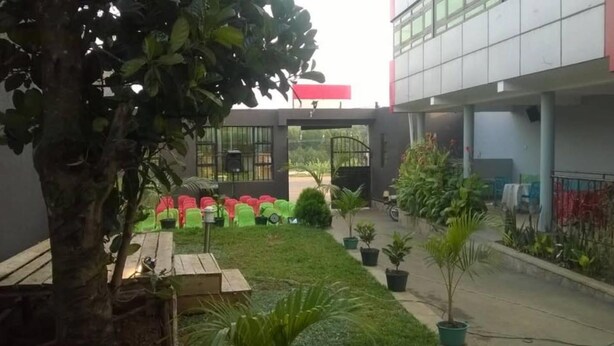 Une cour avec des plantes en pot, un banc en bois et un bâtiment doté de grandes fenêtres et d’un auvent rouge.