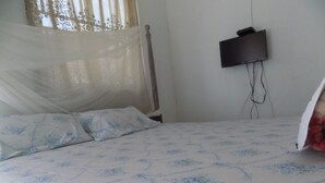 A bed with a floral bedspread, a bedside table, a wall-mounted TV, and a window with sheer curtains. - Sky Resort (Kitagata)