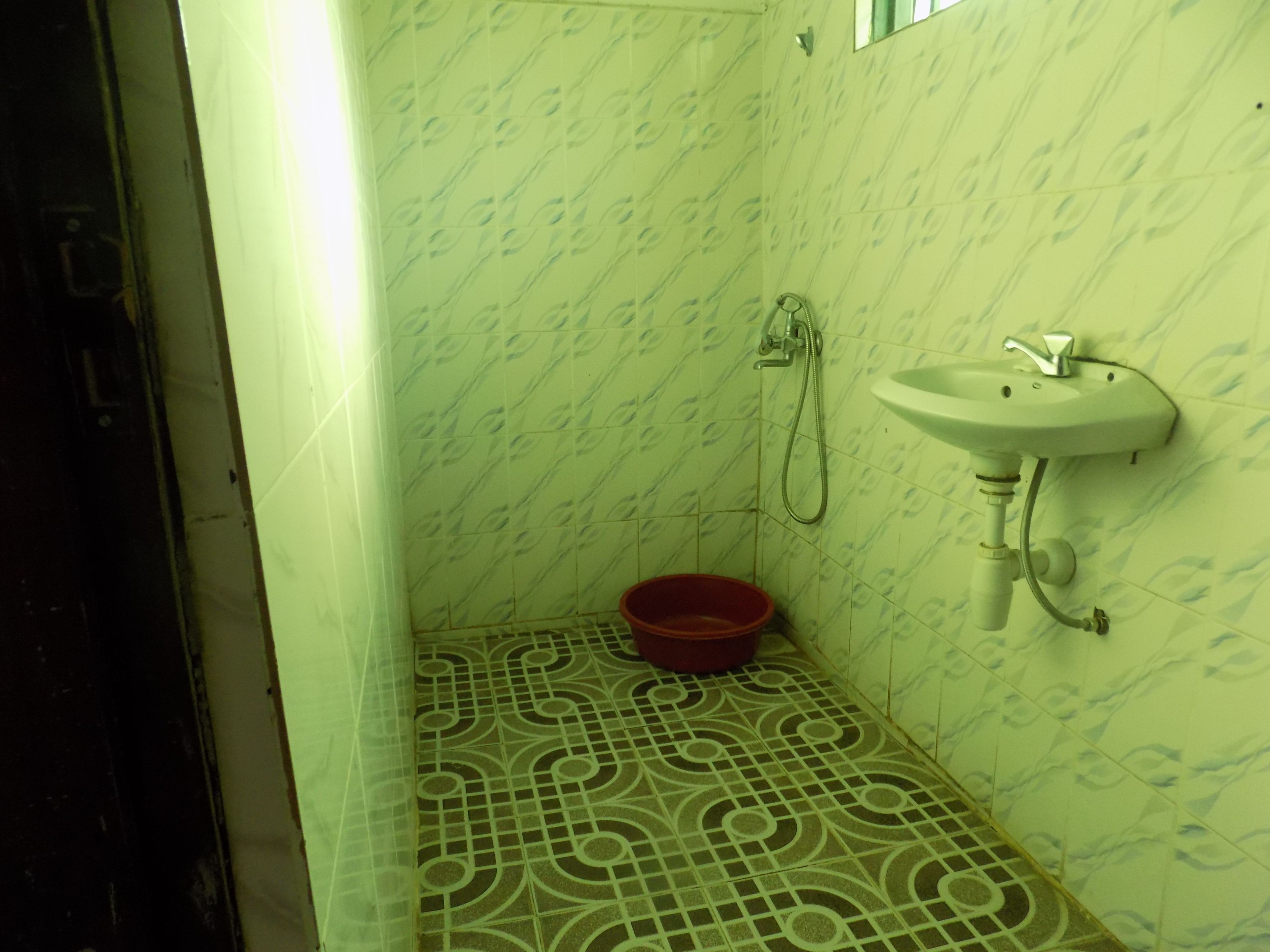A small bathroom with a sink, shower, and a red basin on the floor.