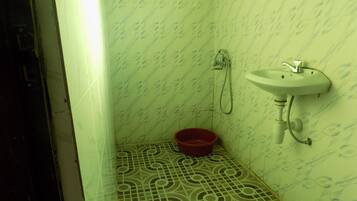A small bathroom with a sink, shower, and a red basin on the floor.