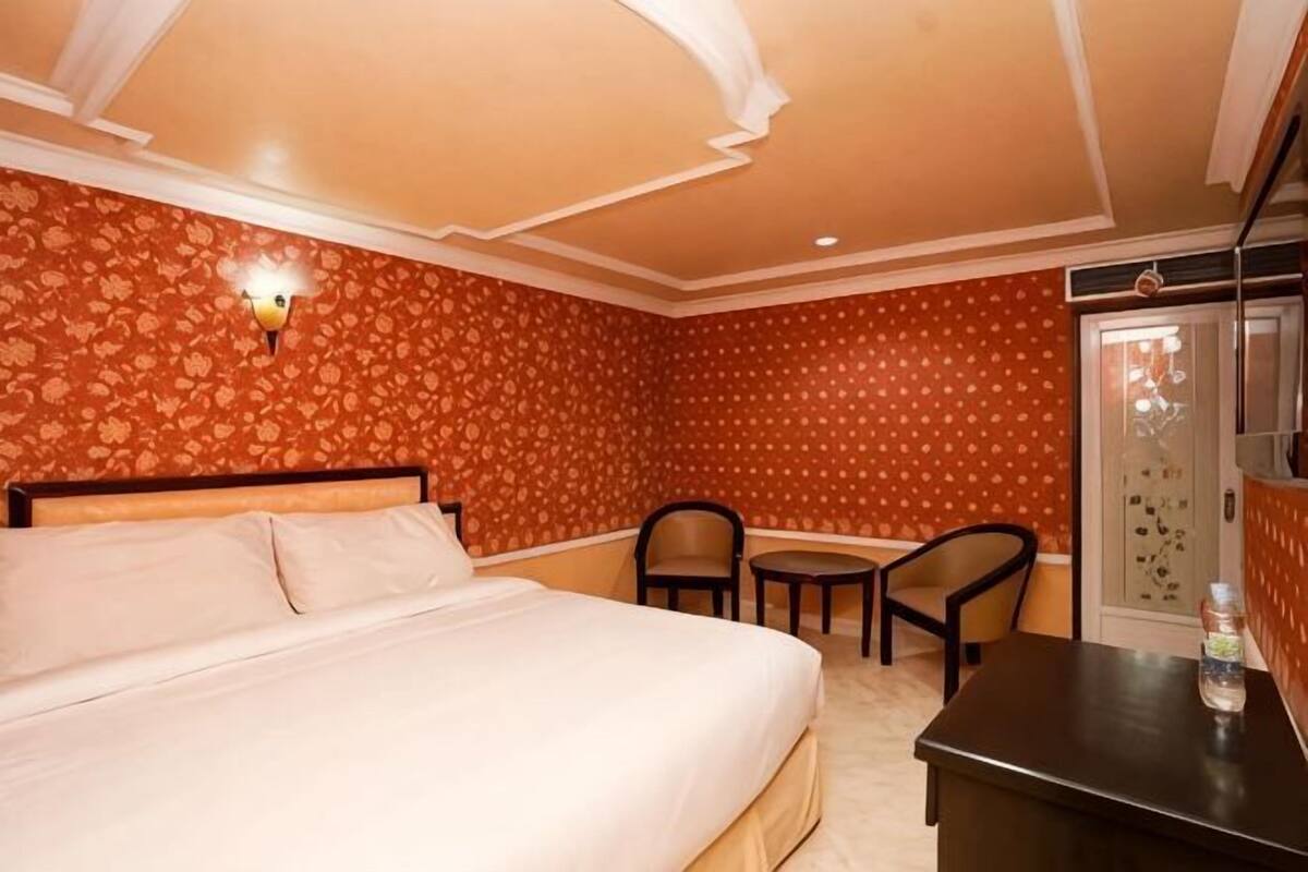 A hotel room with a bed, a desk, a chair, and a small table.